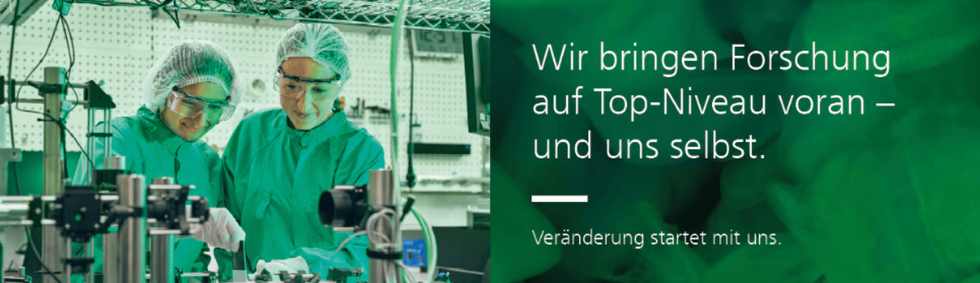 Zwei Wissenschaftler in grüner Schutzkleidung arbeiten mit Laborgeräten. Der Hintergrund besteht aus technischen Geräten und einem grünen Overlay. Der deutsche Text lautet: „Wir bringen Forschung auf Top-Niveau voran – und uns selbst. Veränderung beginnt mit uns.“.