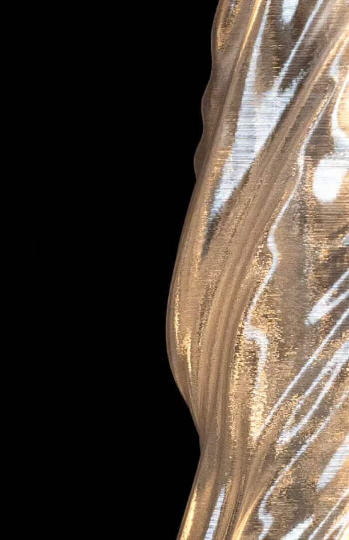 Nahaufnahme einer glatten, metallischen, gold- und silberwelligen Oberfläche mit Lichtreflexionen, die die rechte Seite eines schwarzen Hintergrunds einnimmt.