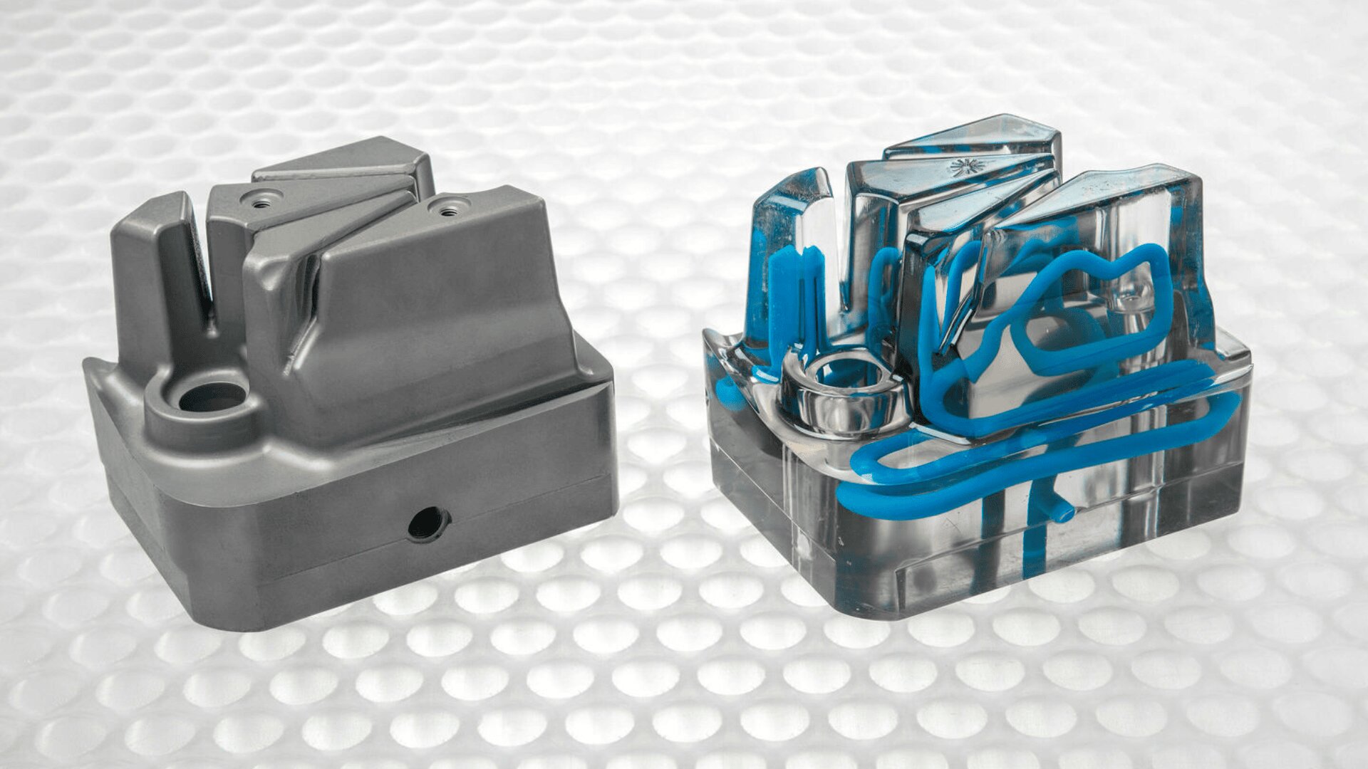 Zwei industrielle Metallformen sind nebeneinander auf einer strukturierten weißen Oberfläche abgebildet. Die rechte Form hat transparente Abschnitte mit sichtbaren blauen Kühlmittelkanälen im Inneren, während die linke Form aus Vollmetall besteht.