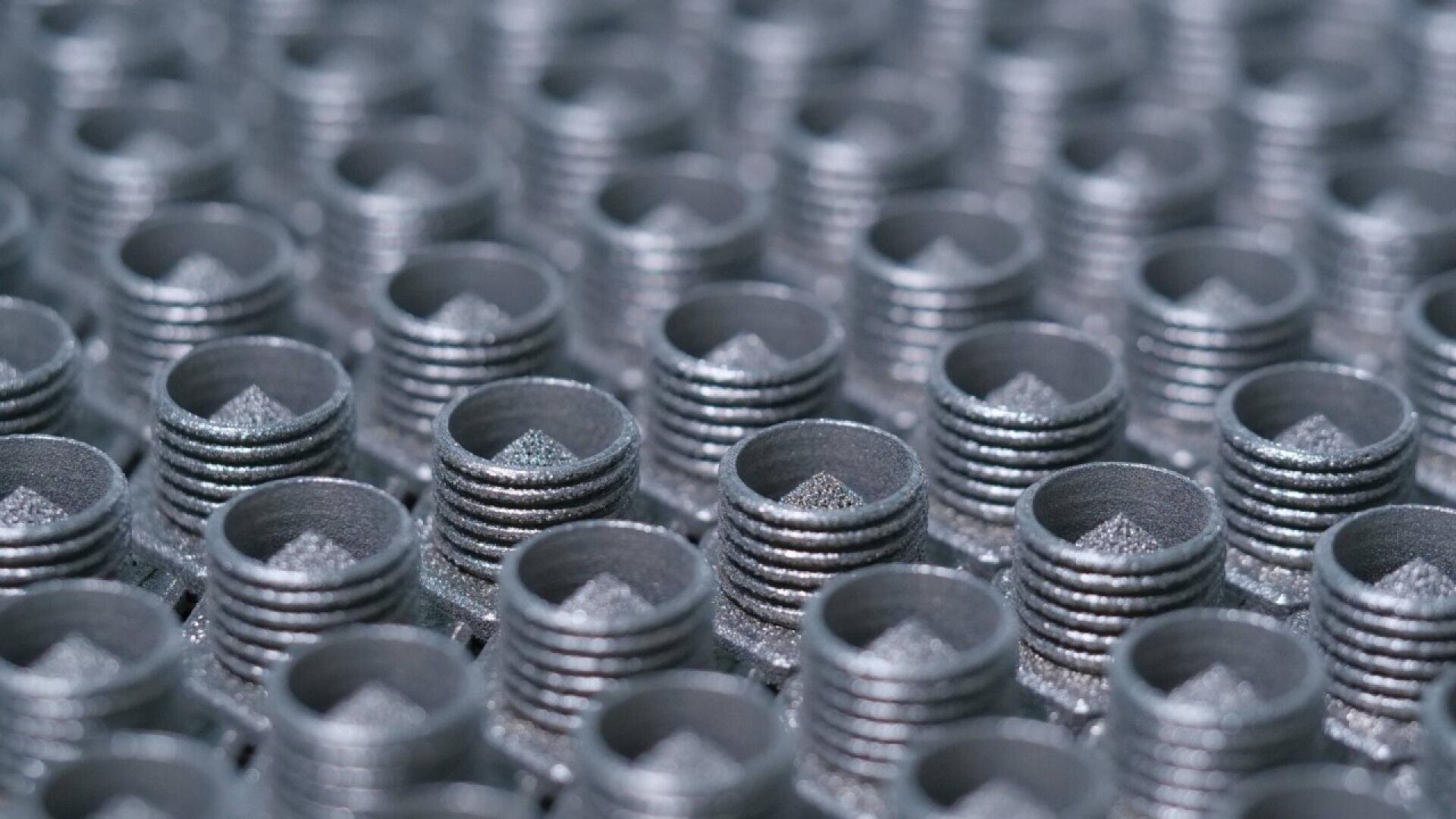 Close-up view of numerous metal threaded inserts arranged in a uniform grid pattern, with a shallow focus highlighting the repeated circular design and metallic texture.
