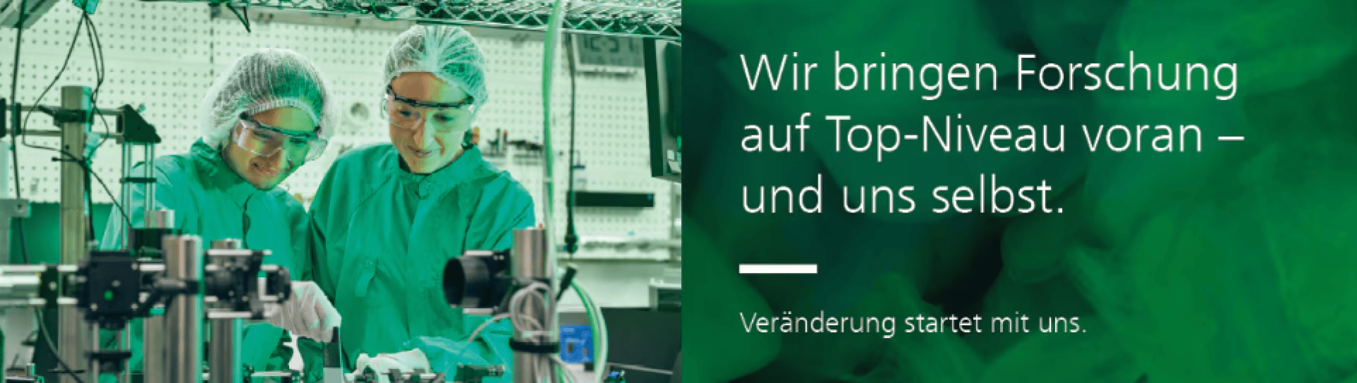 Zwei Forscher in grünen Laborkitteln und Haarnetzen arbeiten mit wissenschaftlichen Geräten in einem Labor. Der deutsche Text lautet: Wir bringen Forschung auf Top-Niveau voran – und uns selbst. Veränderung begann mit uns.