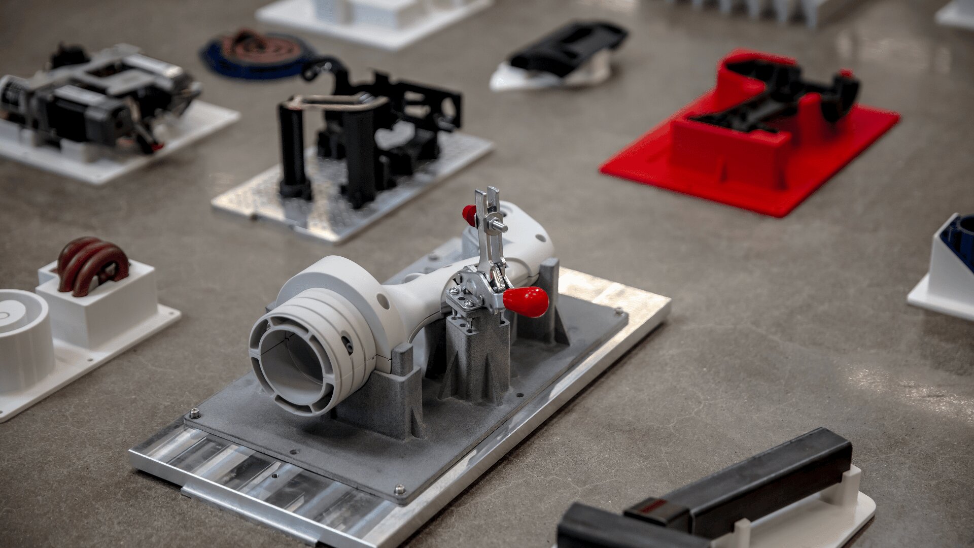 Eine Nahaufnahme verschiedener industrieller und mechanischer 3D-gedruckter Teile in verschiedenen Formen und Farben, dargestellt auf einer grauen Fläche.
