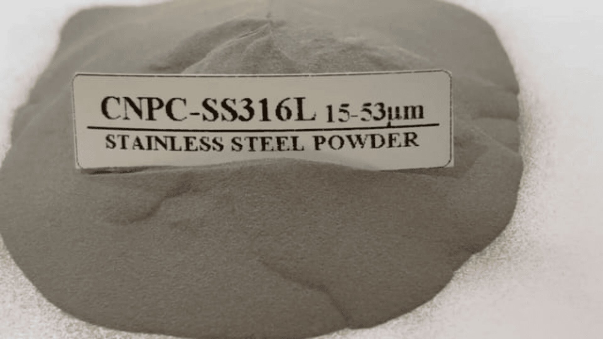 A mound of gray powder with a label reading CNPC-SS316L 15-53μm STAINLESS STEEL POWDER rests on a flat, light-colored surface.