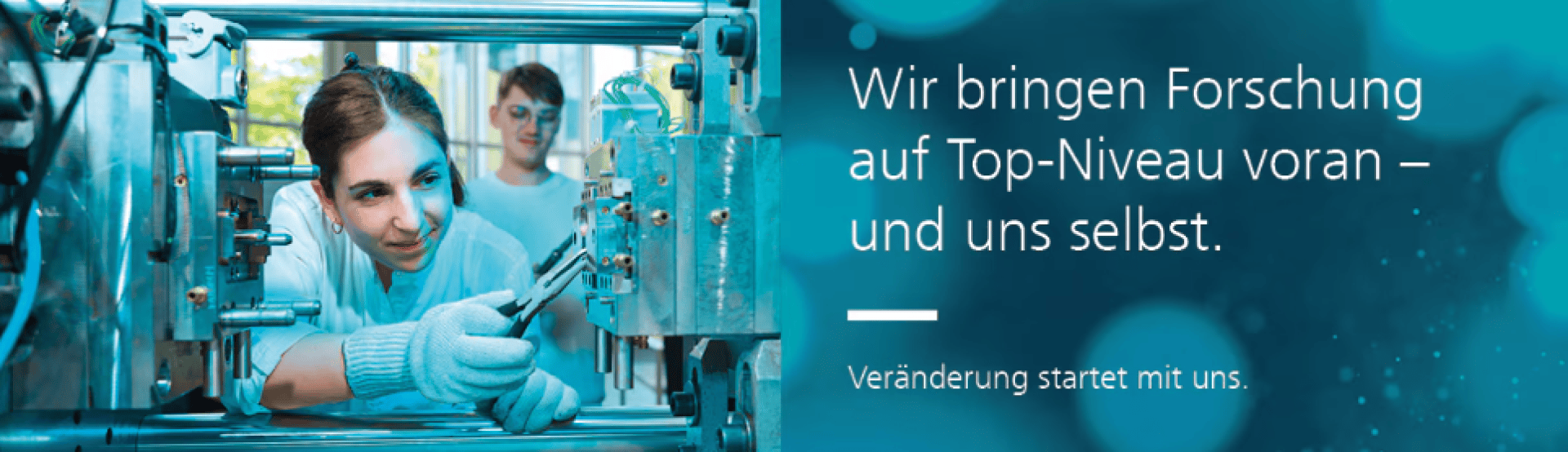 Eine Frau im Laborkittel bedient Werkzeuge an Industriemaschinen, während eine andere Person im Hintergrund zusieht. Der deutsche Text lautet: „Wir bringen Forschung auf Top-Niveau voran – und uns selbst. Veränderung beginnt mit uns.“.