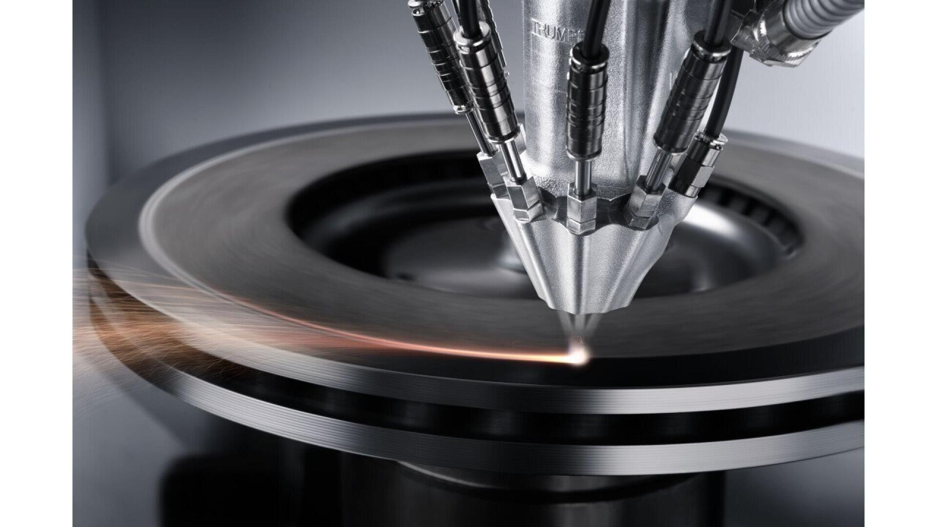 A close-up of a laser welding machine precisely welding or cutting a circular metal component, with sparks visible along the edge where the laser meets the metal surface.