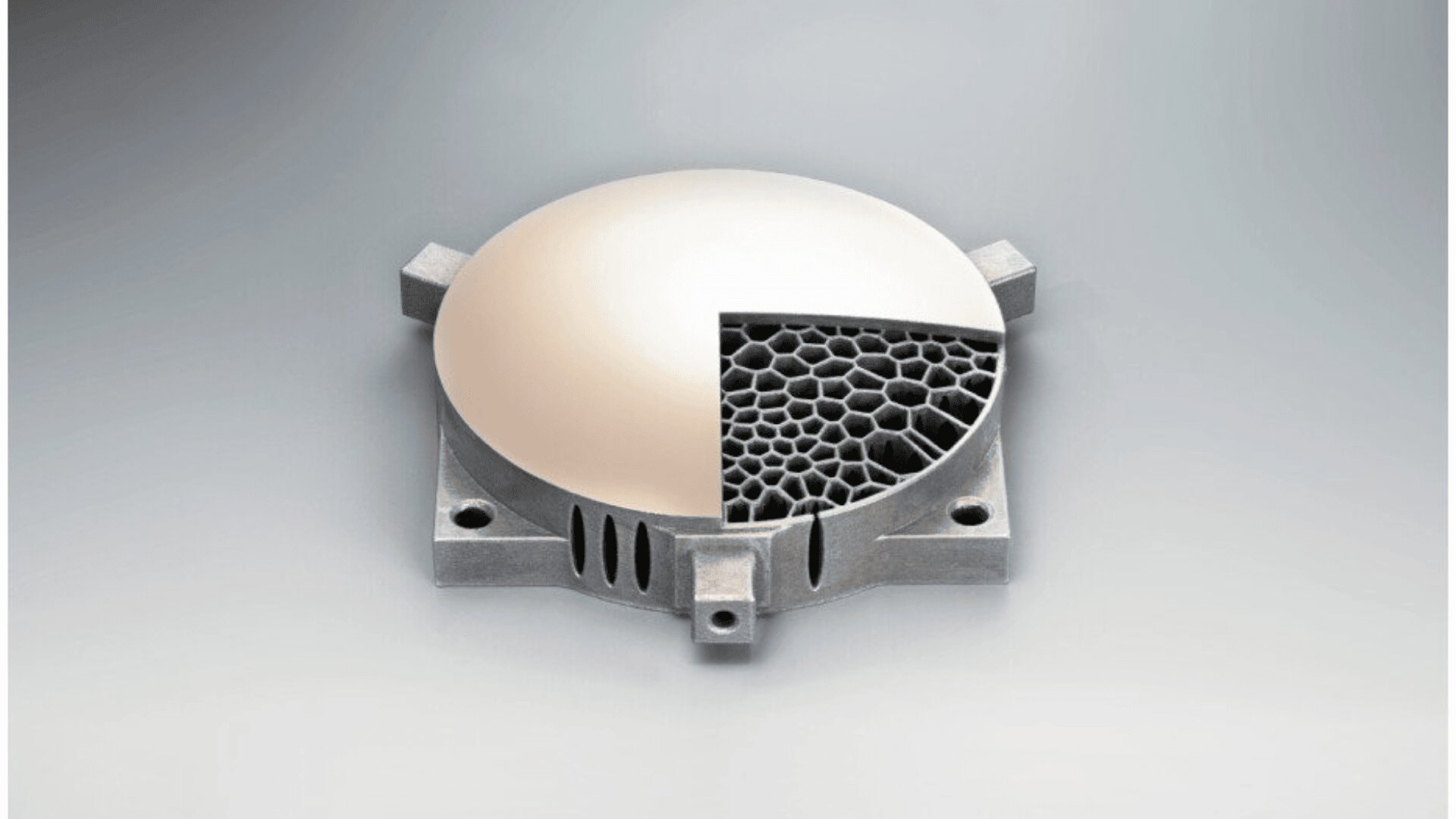 A circular metallic disk with a quarter section removed to reveal a honeycomb-like porous structure underneath, set on a square metallic base with rounded corners.