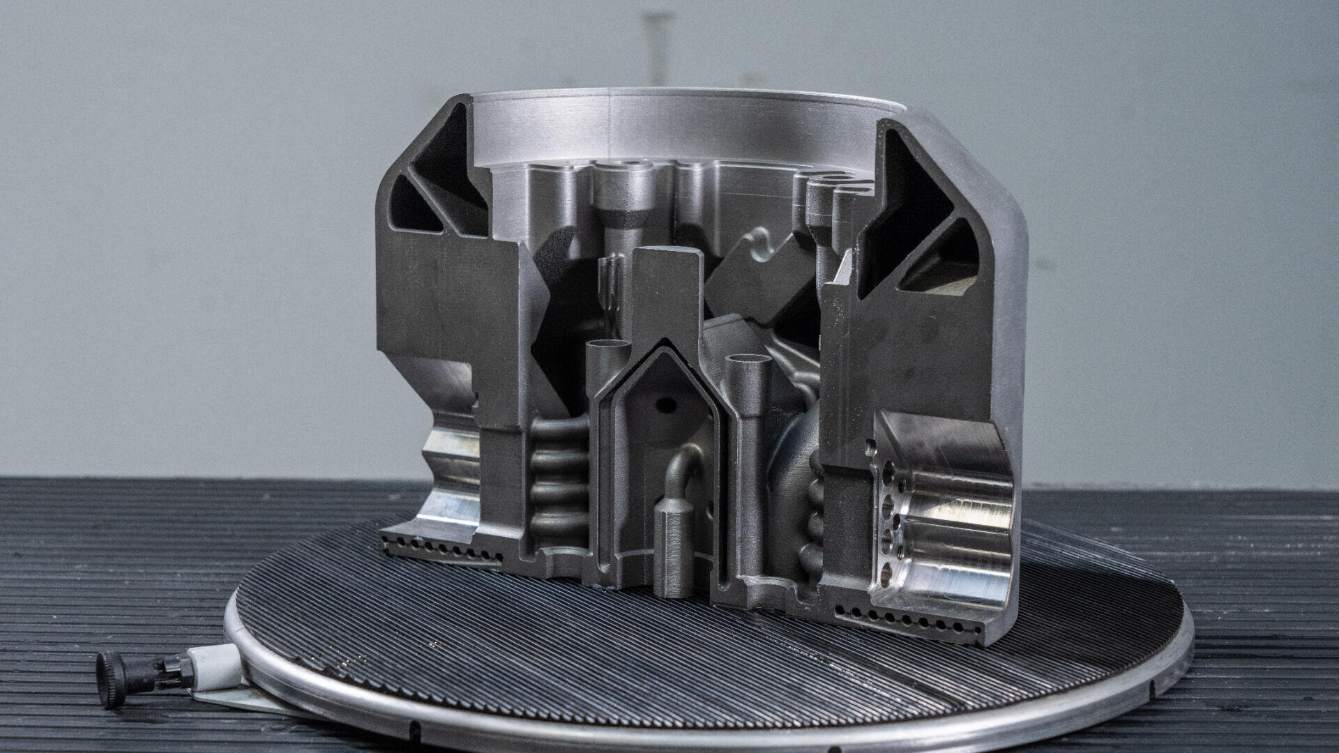 Auf einer kreisförmigen Plattform wird eine metallische mechanische Komponente im Querschnitt präsentiert, wobei die komplexen inneren Kammern und geometrischen Merkmale vor einem neutralen Hintergrund sichtbar werden.