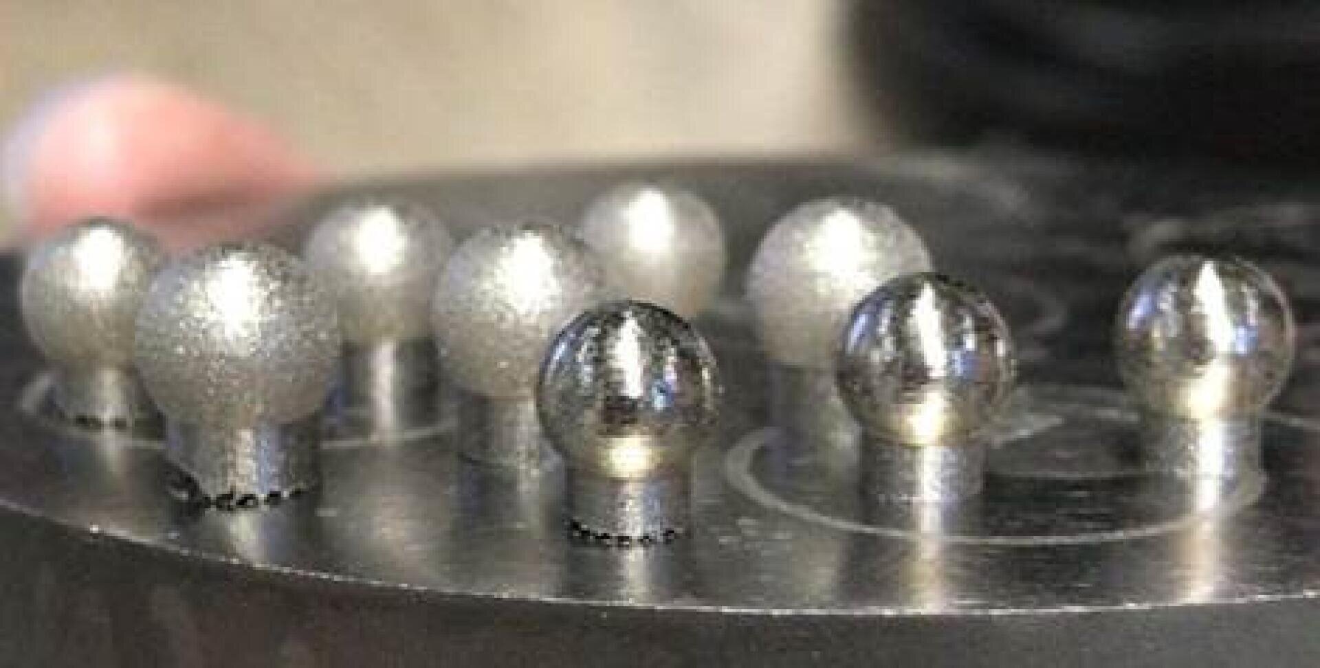 Nahaufnahme von kugelförmigen Metallobjekten, die in zwei Reihen auf einer runden Metallbasis angeordnet sind, mit unterschiedlichen Oberflächenstrukturen und Lichtreflexen.
