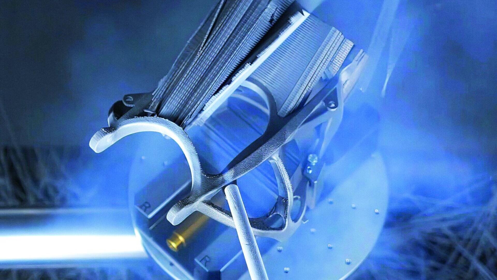 A close-up of a metallic part being manufactured with a 3D printing or metalworking machine, surrounded by blue light and mist, highlighting advanced technology and precision engineering.