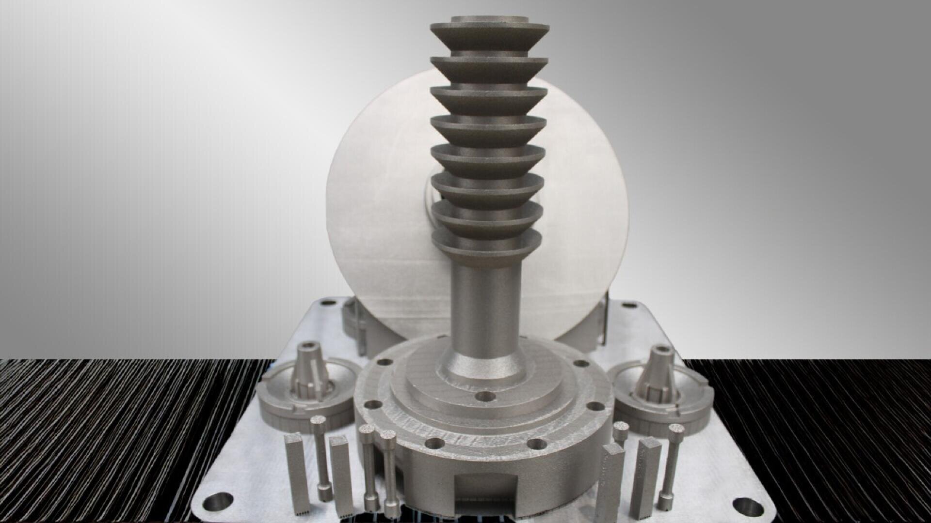 A close-up of a metallic industrial machine component featuring a central spiral-shaped shaft, gear-like base, and symmetrical smaller parts on either side, all set against a gradient gray background.