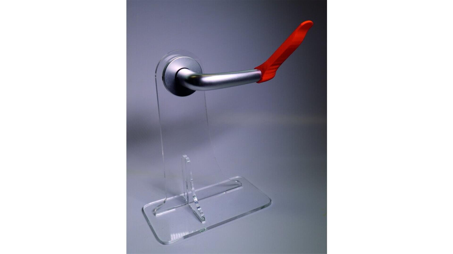 A metallic door handle with a red attachment is mounted on a transparent acrylic display stand against a plain background.