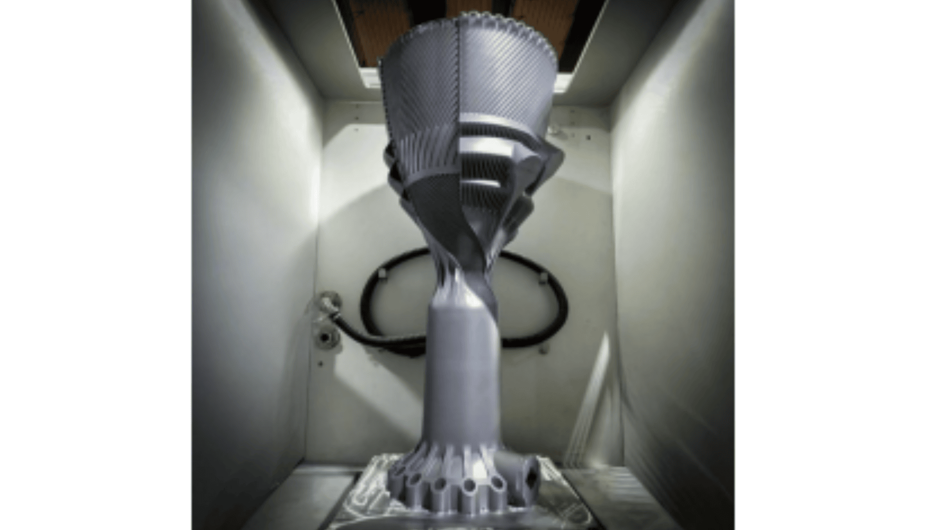 In einem weißen Gehäuse wird eine große, komplizierte metallische 3D-gedruckte Raketentriebwerkskomponente ausgestellt, die detaillierte geometrische Muster und moderne Technik hervorhebt.