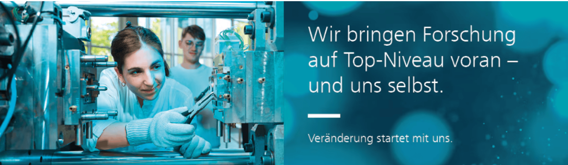 Eine junge Frau im Laborkittel bedient Werkzeuge an Industrieanlagen, während ein Kollege zusieht. Der deutsche Text lautet: Wir bringen Forschung auf Top-Niveau voran – und uns selbst. Veränderung begann mit uns.