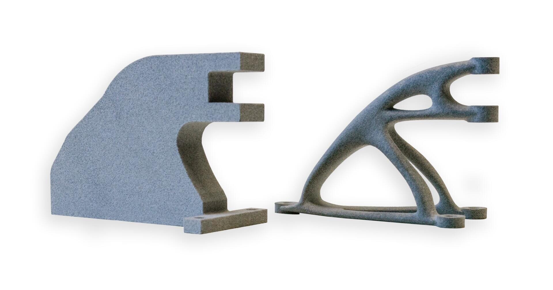 Zwei graue, 3D-gedruckte mechanische Teile werden nebeneinander gezeigt. Der linke Teil ist massiv und blockartig, während der rechte Teil leicht ist und ein gitter- und fachwerkartiges Design aufweist, was eine strukturelle Optimierung veranschaulicht.