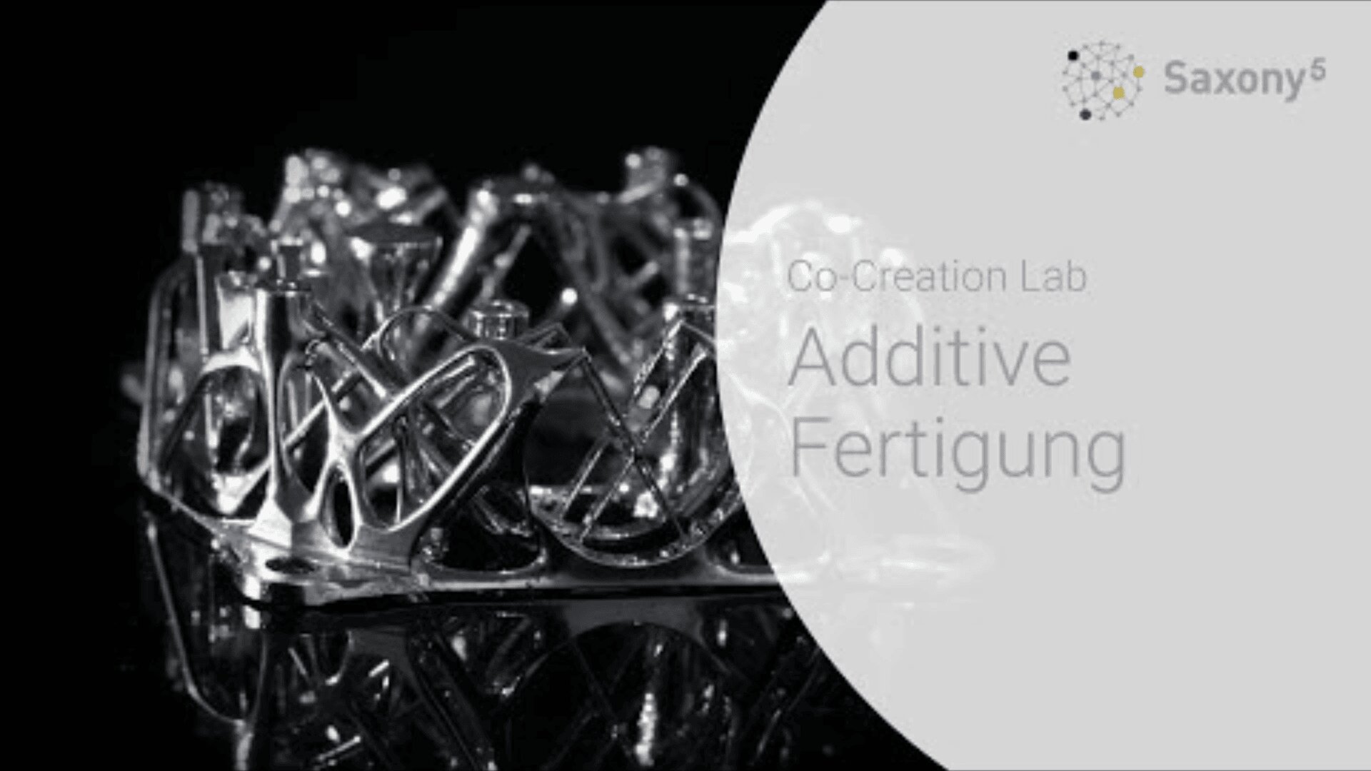 Eine glänzende, filigrane 3D-gedruckte Metallstruktur sitzt auf einer reflektierenden schwarzen Oberfläche. Rechts steht der Text „Co-Creation Lab Additive Fertigung“ mit einem Saxony5-Logo darüber.