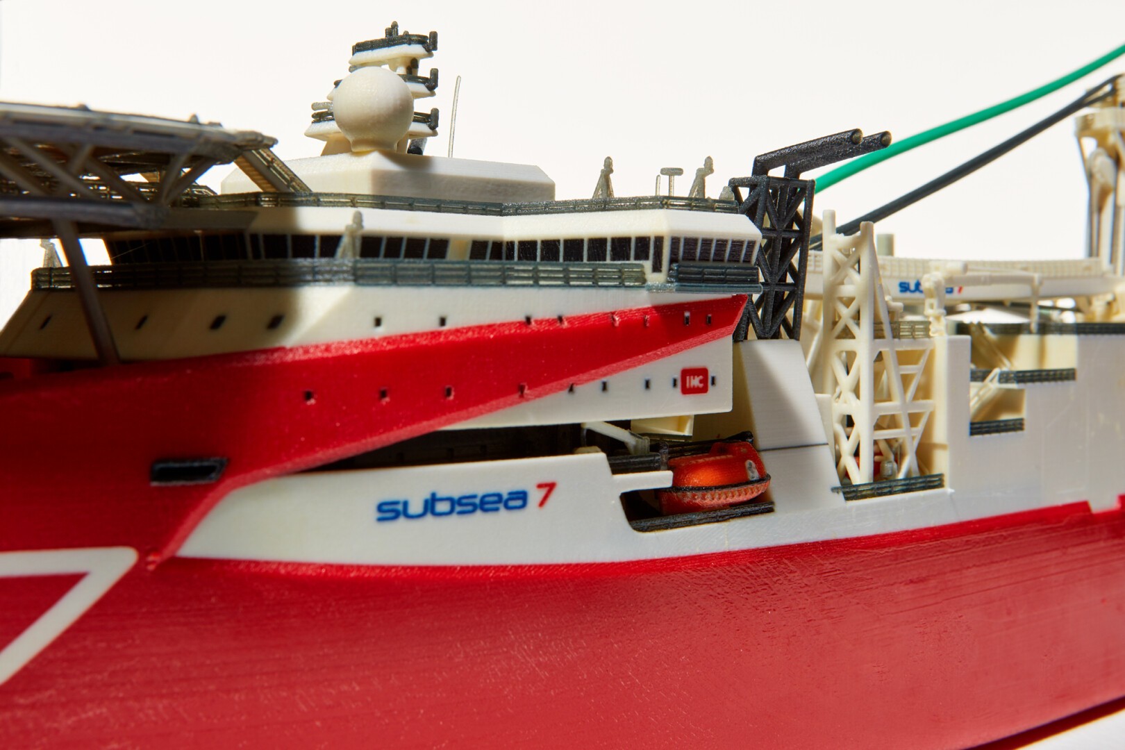 Nahaufnahme eines detaillierten Schiffsmodells mit rot-weißem Rumpf, seitlich mit der Aufschrift „Subsea 7“ gekennzeichnet, und komplizierten Strukturen und Ausrüstung auf dem Deck.