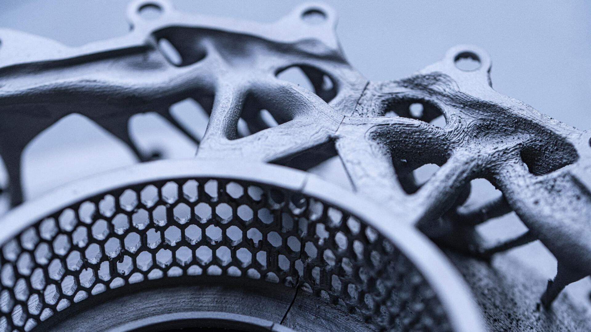 Nahaufnahme eines metallischen, 3D-gedruckten mechanischen Teils mit komplizierten Gitterstrukturen und sechseckigem Maschenmuster, das komplexe Konstruktions- und moderne Fertigungstechniken zeigt.