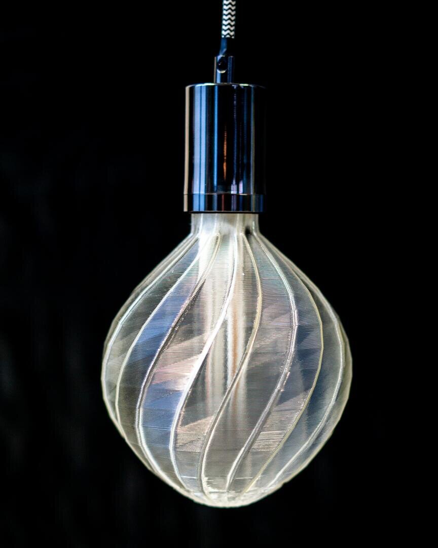 Eine moderne, dekorative Glühbirne mit spiralförmigem Glasdesign hängt an einer Schnur vor einem schwarzen Hintergrund. Die Glühbirne leuchtet und strahlt einen sanften Schein aus.