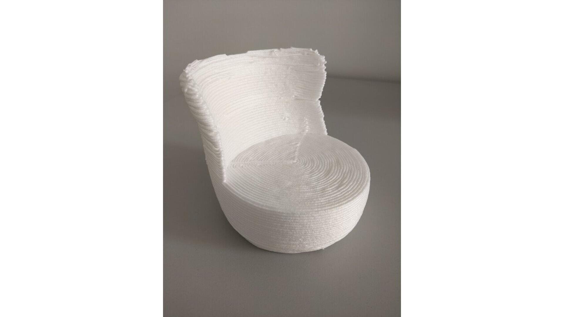 A small white chair with a curved back and textured, layered surface, resembling it was made using a 3D printing process, placed on a plain gray background.