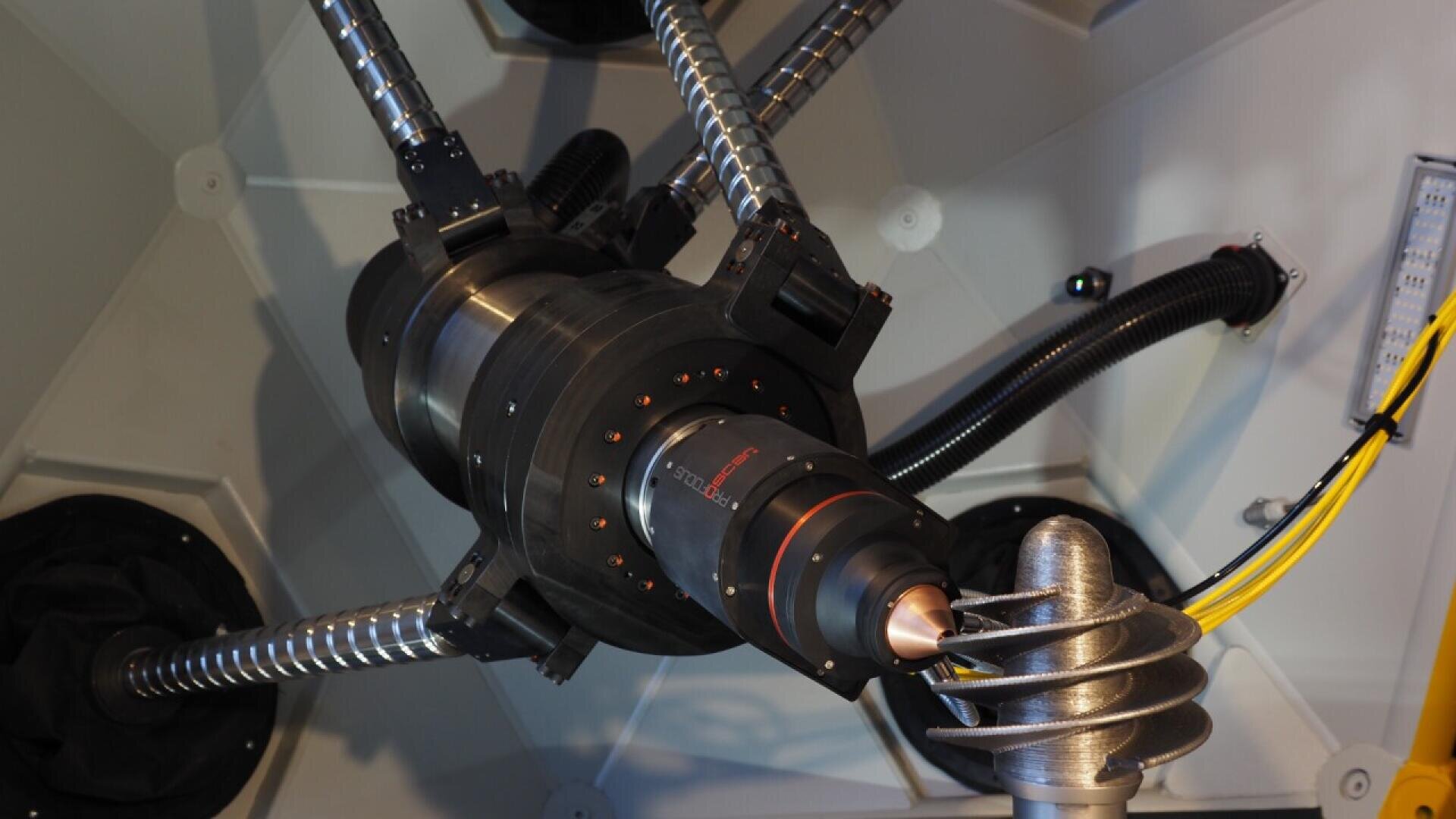 A close-up view of a mechanical device with metal rods, black cylindrical components, and coiled tubing inside a white enclosure, featuring various cables and connectors.