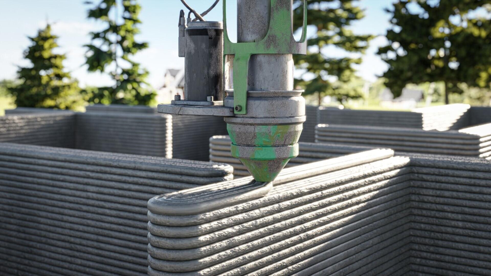 A close-up of a 3D printer nozzle constructing a building wall by extruding concrete in horizontal layers, with trees and a clear sky visible in the background.