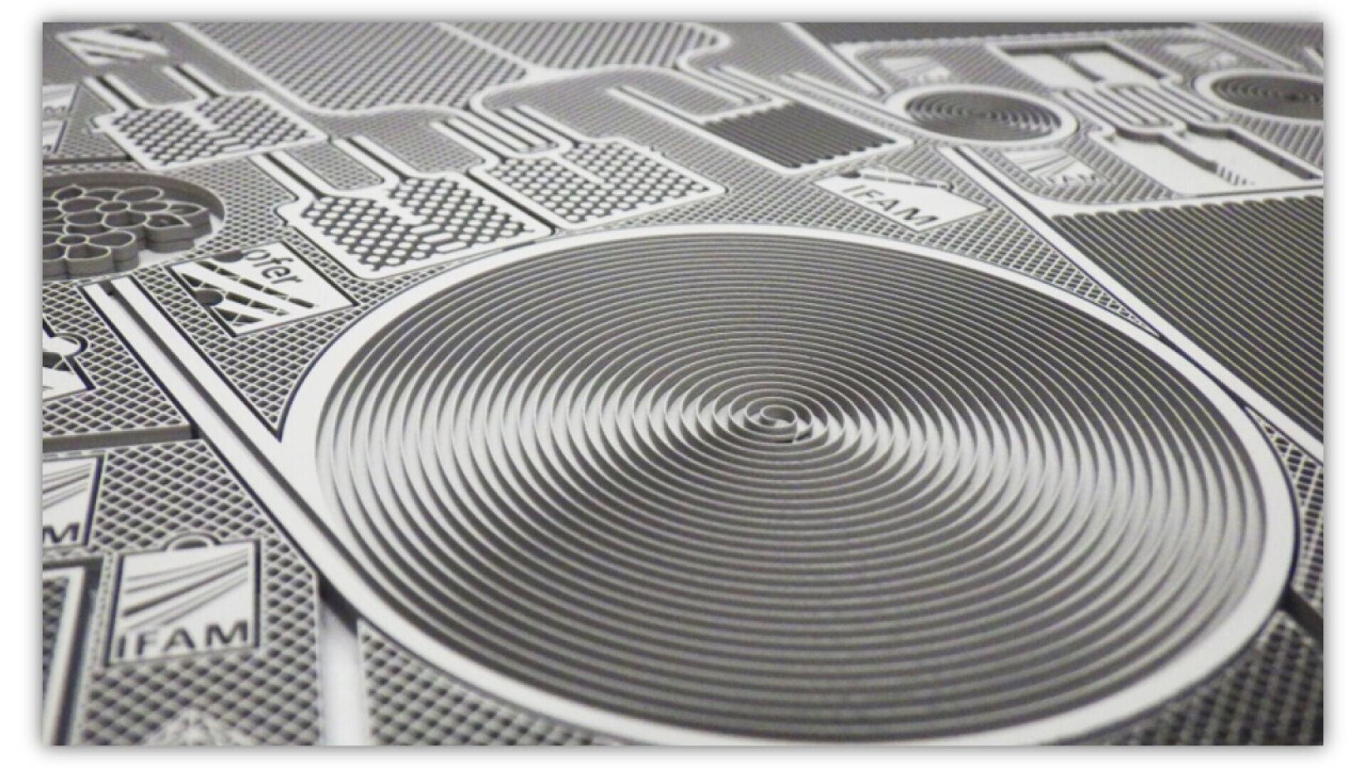 Close-up view of a printed circuit board (PCB) design with intricate, etched lines, circular shapes, and geometric patterns in shades of black, white, and gray.