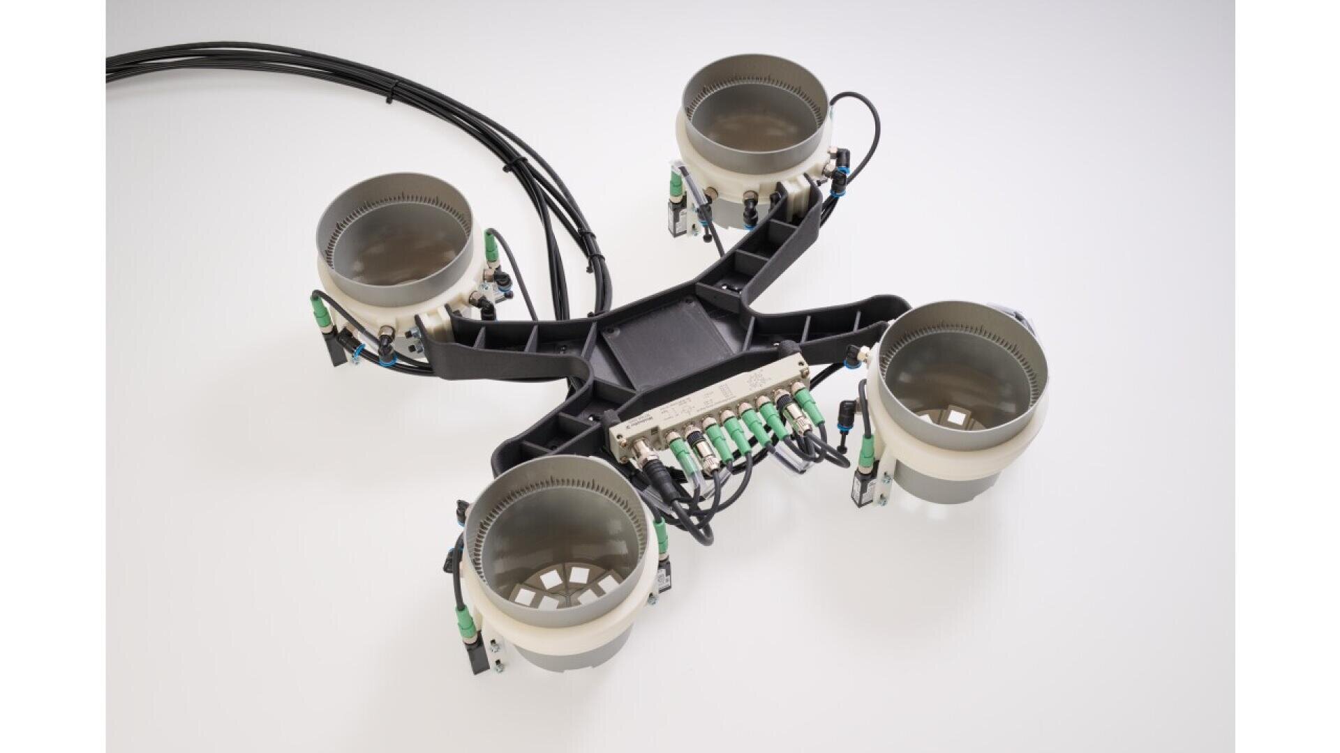A close-up of a black and gray quadcopter drone frame with four circular mounts and several wires and connectors attached, set on a plain white background.