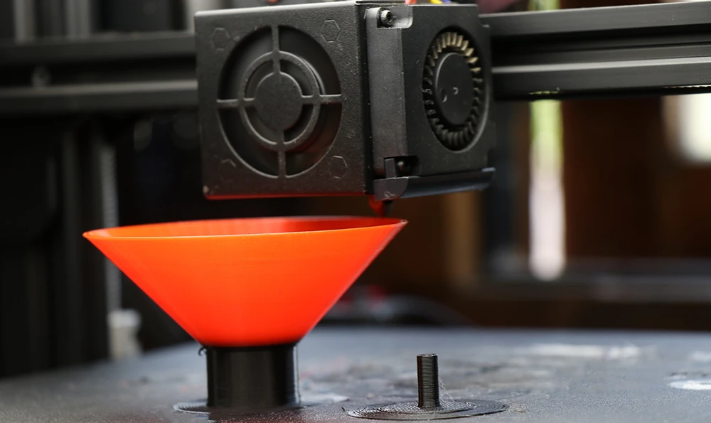 A 3D printer currently printing an orange funnel.